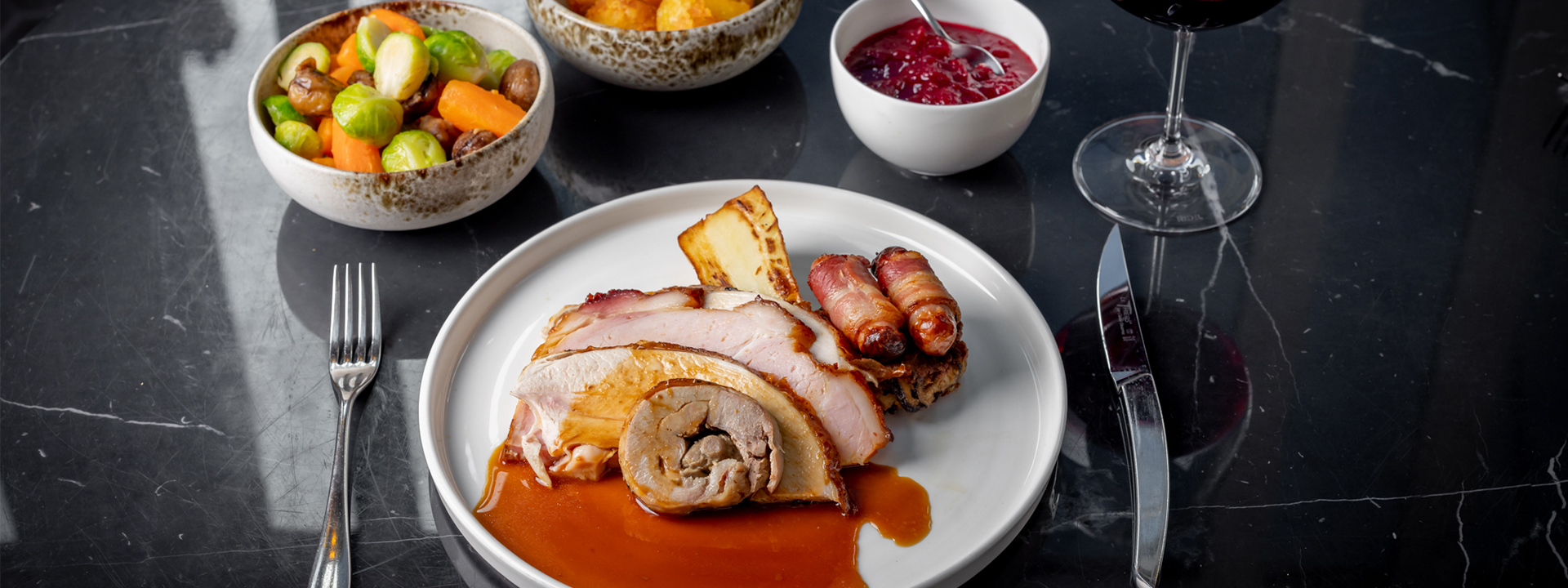 Meat with assortment of side dishes served on a black table with a glass of red wine