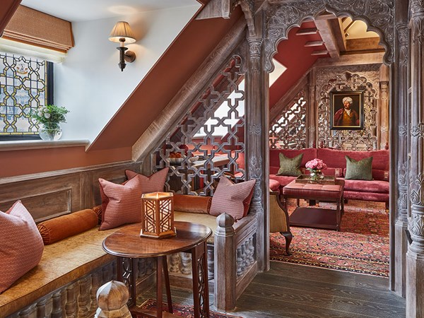 The King's Lodge interior with a seating area covered in cushions, and through the wooden structure a living area with red sofas and a portrait hanging up on the wall